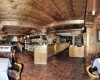 Reštaurácia s drevenými stropmi a nábytkom, prestreté stoly a bar v pozadí.