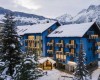Modrý hotel obklopený zasneženými horami a stromami.