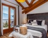 Spálňa s manželskou posteľou, výhľadom na hory, drevenými trámami a moderným dekorom.