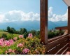 Drevený balkón s kvetmi a výhľadom na hory s modrou oblohou a oblakmi.