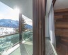 Výhľad z okna na zasnežené hory a balkón so skleneným zábradlím.