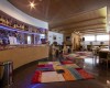 Interiér reštaurácie s barom, farebnými kobercami a drevenými stolmi so stoličkami.
