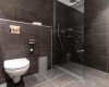 Moderná kúpeľňa s toaletou, sprchou a tmavými dlaždicami.  