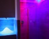 Moderný sprchový kút s farebným osvetlením v odtieňoch modrej a fialovej.  