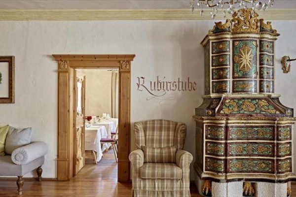 Historická kachľová pec vedľa prúteného kresla v rustikálnom interiéri s nápisom 