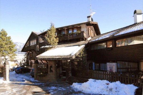 Drevený horský hotel s parkovacími miestami, obklopený snehom a stromami.