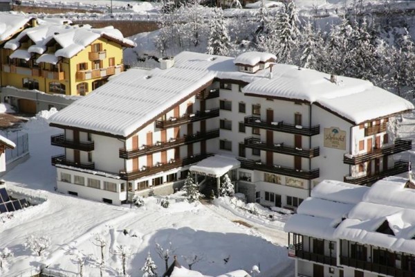 Zasnežený horský hotel obklopený ďalšími budovami v zasneženej krajine.