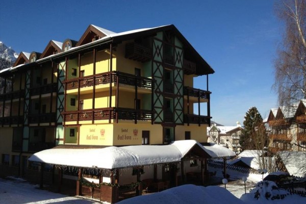 Viacposchodový hotel s drevenými balkónmi, zasnežená strecha, modré nebo v pozadí.