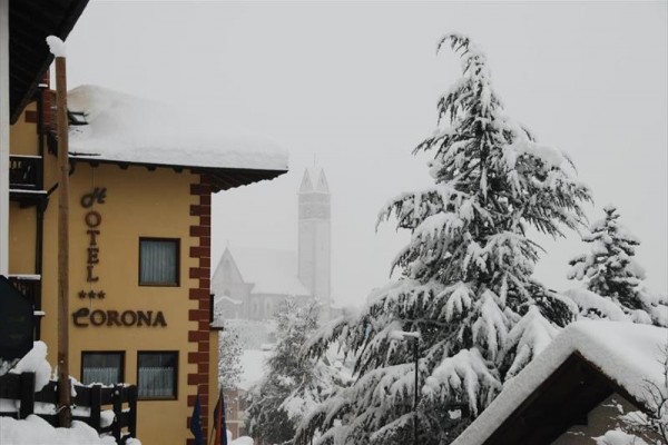 Snehom pokrytá krajina s hotelom a kostolnou vežou v pozadí.