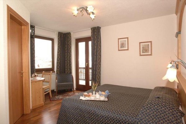 Hotelová izba s manželskou posteľou, stolom a francúzskymi dverami na balkón.