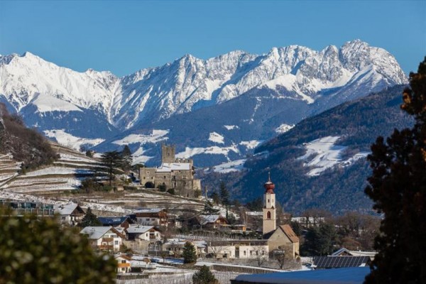 Zasnežené horské mesto s kostolom a hradom v pozadí.