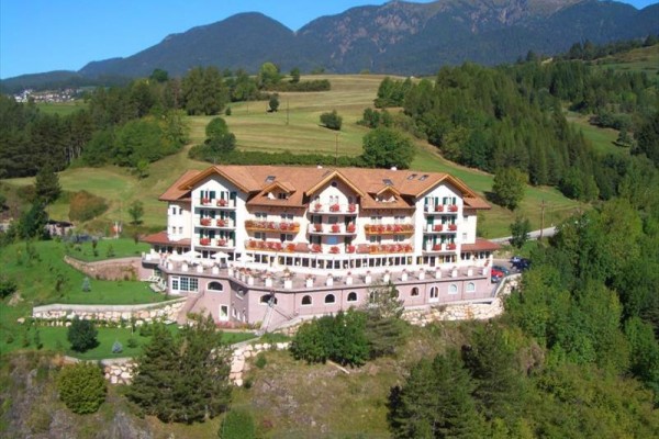 Hotel obklopený zeleňou a horami v pozadí.  