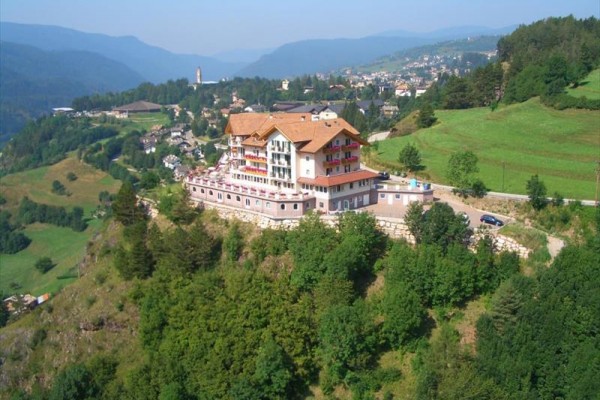 Hotel na vrchole kopca obklopený zelenou krajinou a kopcami v pozadí.