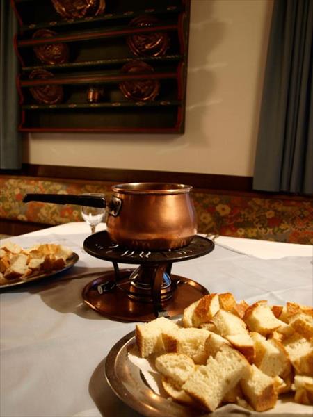 Medený hrniec na fondue s taniermi kociek chleba na stole.