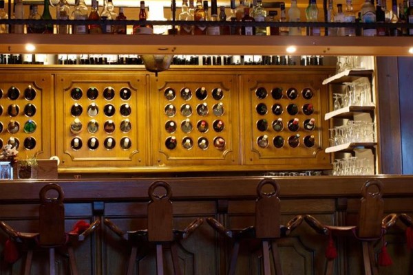 Drevený bar s policami plnými fliaš alkoholu a pohármi na víno.