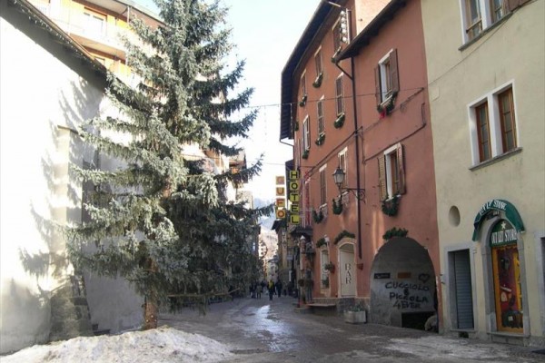 Úzka ulica s hotelom, stromčekom a snehom na zemi.