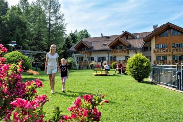 Žena s dieťaťom prechádza záhradou pri horskom penzióne s výhľadom na ihrisko.
