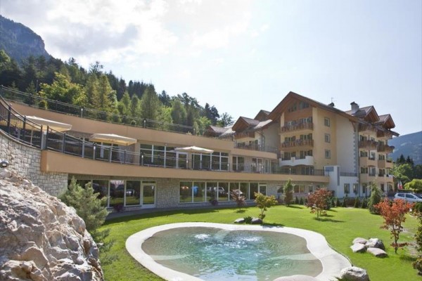 Moderný hotel so záhradou a malým jazierkom obklopený lesom.