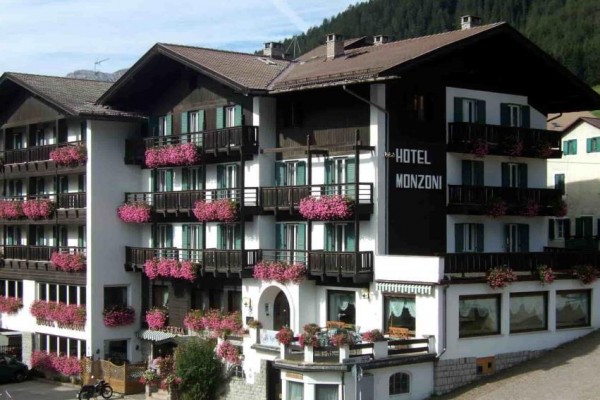 Hotel s drevenými balkónmi zdobenými ružovými kvetmi.