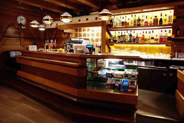Drevený bar s osvetlenými policami plnými fliaš alkoholu a vitrínou so sladkosťami.