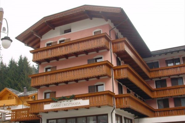 Štvorposchodový horský hotel s drevenými balkónmi a ružovou fasádou.
