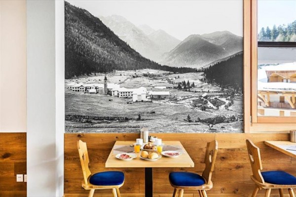 Stôl s raňajkami v reštaurácii s veľkou čiernobielou fotografiou alpskej krajiny na stene.