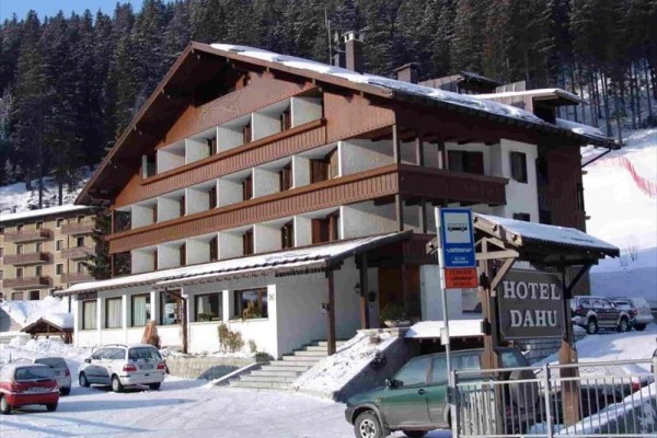 Dvojposchodový horský hotel v zasneženej krajine s parkoviskom a okolitými stromami.