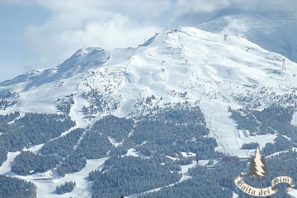 Zasnežená horská krajina s lesmi a lyžiarskymi zjazdovkami.