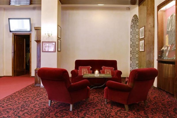 Kút s červenými kreslami a pohovkou v elegantnom interiéri s kobercami a sviečkou na stolíku.