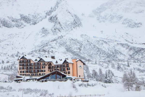 Hotel obklopený zasneženými horami a stromami v zimnej krajine.