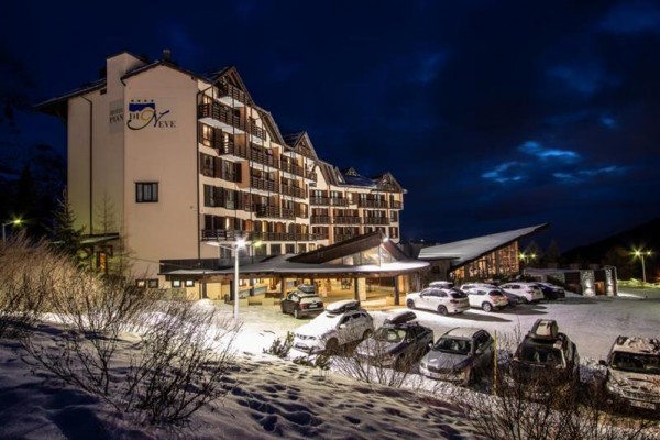 Hotel s osvetleným parkoviskom v zimnej krajine pri súmraku.