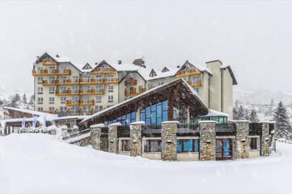 Horský hotel pokrytý snehom s drevenými balkónmi.