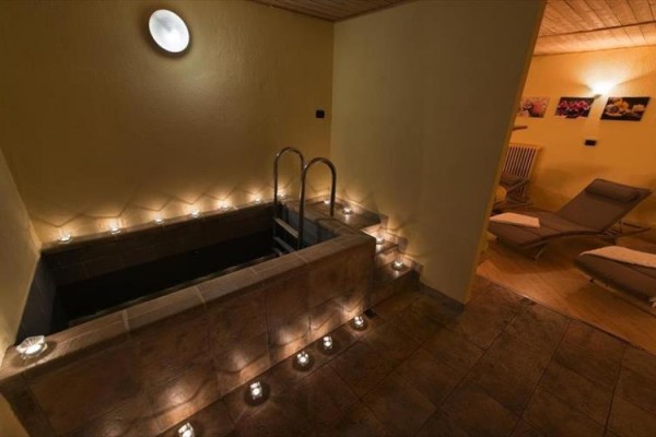 Malý bazén s kovovým rebríkom, obklopený sviečkami v miestnosti s dvoma lehátkami.  