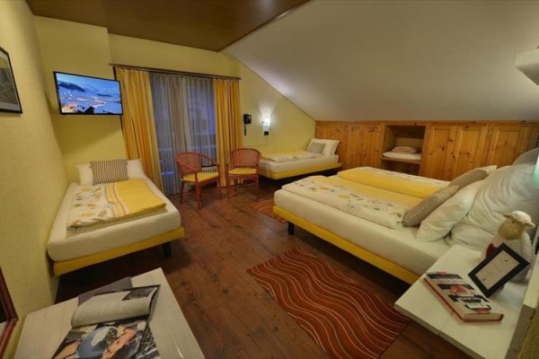 Ubytovacia izba s tromi posteľami, drevenými stenami a televízorom.
