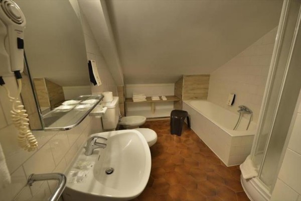 Kúpeľňa s vaňou, sprchovacím kútom, umývadlom, WC a policou s uterákmi pod šikmým stropom.