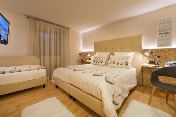 Moderná spálňa s manželskou posteľou a vedľajším lôžkom, na zemi svetlý koberec.