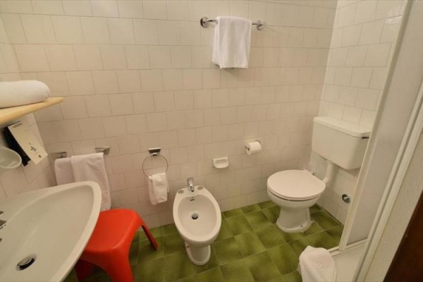 Kúpeľňa s umývadlom, bidetom, toaletou, zelenou podlahou a červenou stoličkou.  