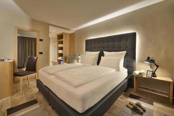 Moderná hotelová izba s veľkou posteľou, nočnými stolíkmi a šatníkom.