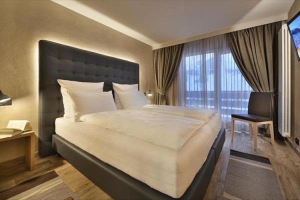 Moderná hotelová izba s veľkou posteľou a oknom so závesmi.