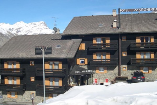 Horský hotel s drevenými balkónmi zasadený do zasneženej alpskej krajiny.