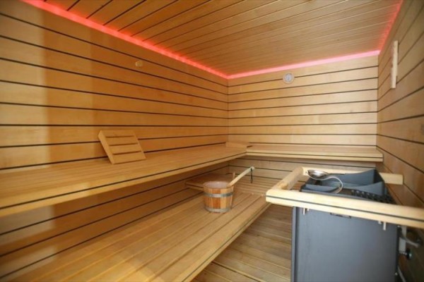 Drevená sauna s lavičkou a kachľami, lemovaná červenými LED svetlami.