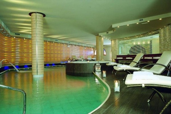 Luxusný interiér wellnessu s bazénom, lehátkami a sviečkami.