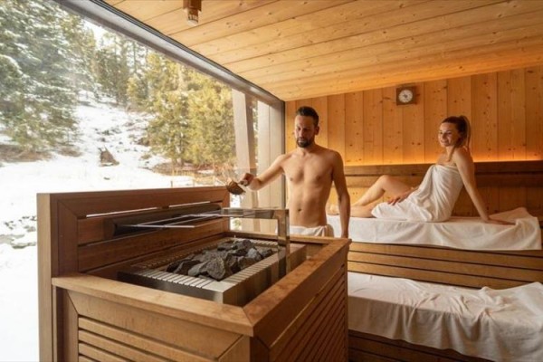 Dvaja ľudia relaxujú v drevenej saune s výhľadom na zasneženú krajinu.