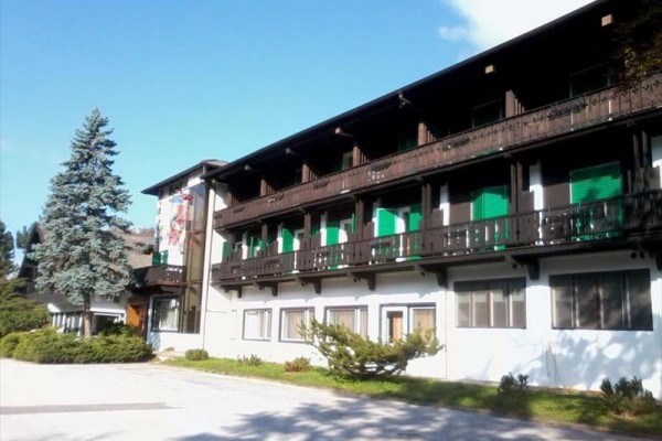 Veľká budova s drevenými balkónmi a zelenými okenicami pod modrou oblohou.