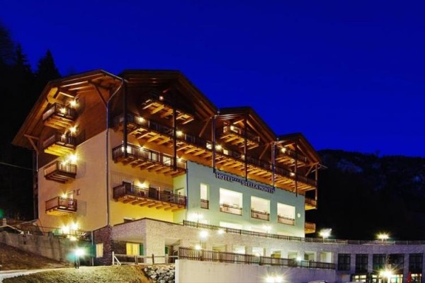 Osvetlený hotel s drevenými balkónmi na horskom svahu za súmraku.