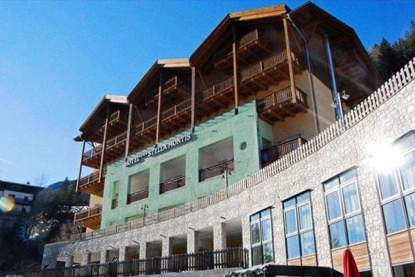 Hotel s terasami a drevenými balkónmi pod modrou oblohou.