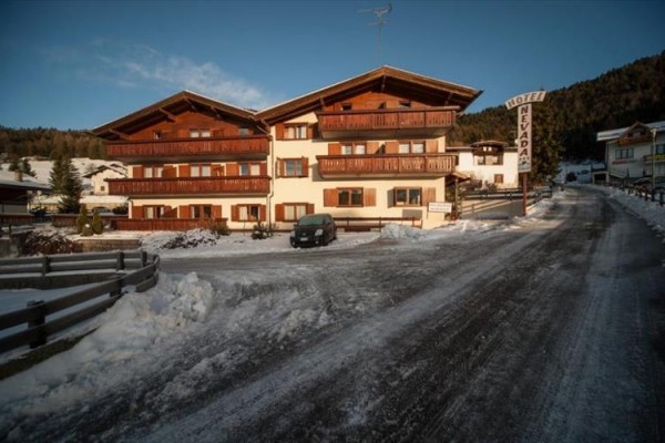 Zasnežená cesta vedie k horskému hotelu s drevenými balkónmi.