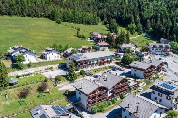 Horské mestečko obklopené lesmi s domami a solárnymi panelmi na strechách.