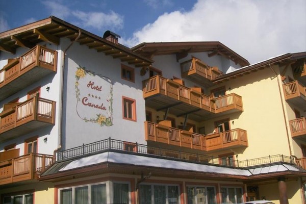 Hotel s drevenými balkónmi a maľbou kvetov na stene pod modrou oblohou.