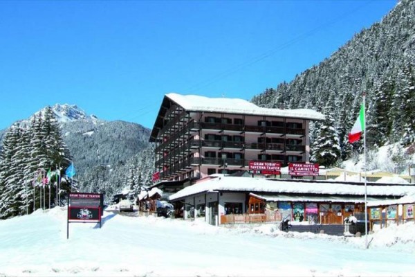 Hotel v zasneženej horskej krajine s talianskou vlajkou v popredí.